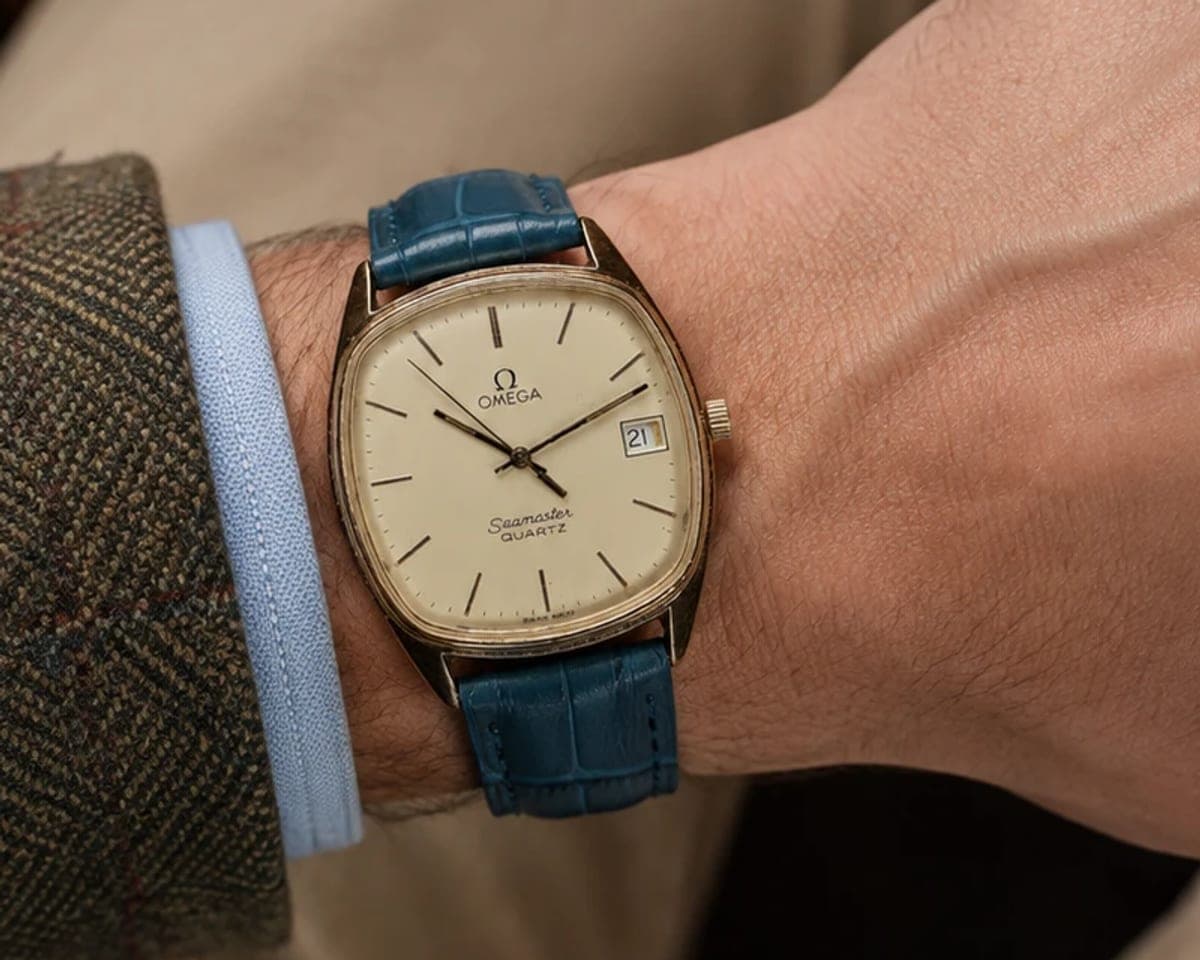 A gold Omega Seamaster on a teal strap, worn on the wrist